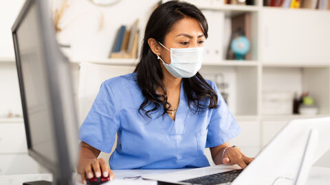 Arzthelferin mit Maske arbeitet am PC Arzthelferin mit Maske arbeitet am PC