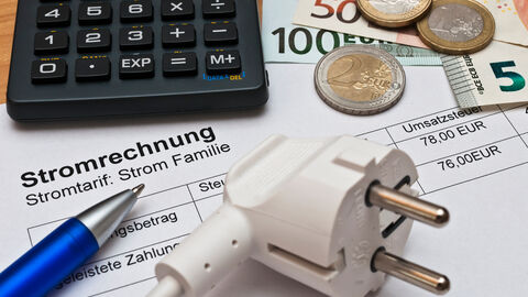 Ein Steckdosenstecker liegt auf Papier und neben einem Taschenrechner und Münzgeld.