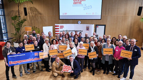 Neue Engagements-Lotsinnnen und Lotsen  Staatsminister Axel Wintermeyer gemeinsam mit allen neuen Engagements-Lotsinnnen und Lotsen. Die Lotsinnen und Lotsen halten Bilder von Ortsschildern.