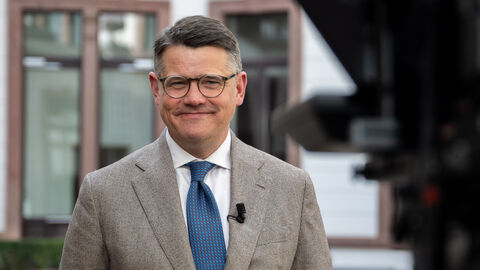 Ein Mann im braunen Anzug mit Brille und einer blauen Krawatte