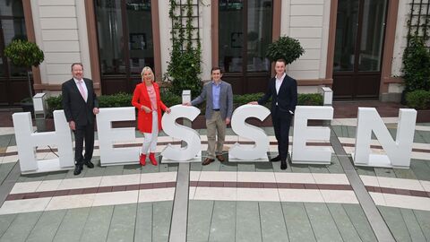 Eine Frau und zwei Männer stehen zwischen Buchstaben, die das Wort "Hessen" ergeben.