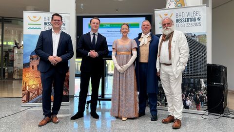 Programmvorstellung Hessentag Eine Gruppe Personen steht zusammen vor Aufstellern des Hessentags in Bad Vilbel.