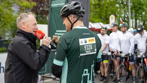 Radklassiker Eschborn-Frankfurt Ministerpräsident Rhein in seinem Raddress neben einem Mann mit Mikrofon, beide unterhalten sich