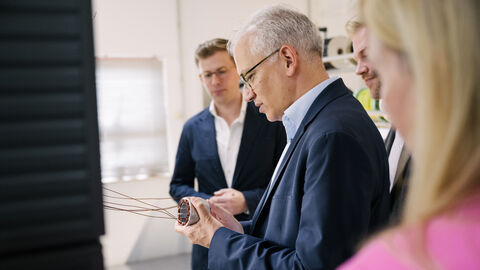 Al-Wazir hält ein Metallteil in Händen und begutachtet es, um ihn weitere Personen.