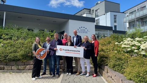 Mehrere Personen stehen vor Klinik und halten ein Schild in Kamera.